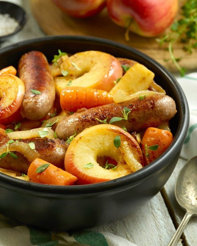 a bowl filled with sausages, apples and carrots on top of a table