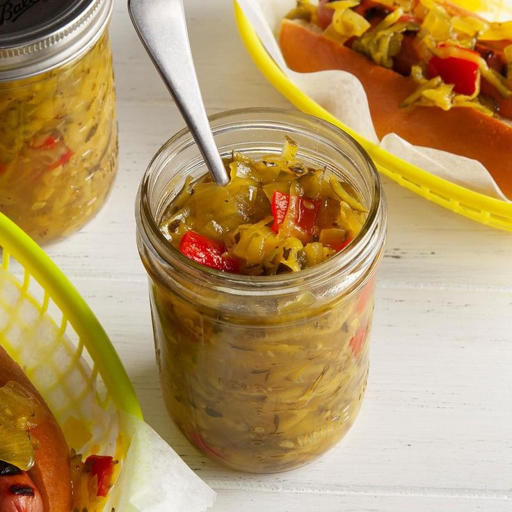 hotdogs and pickles in a jar with a spoon on the table next to them