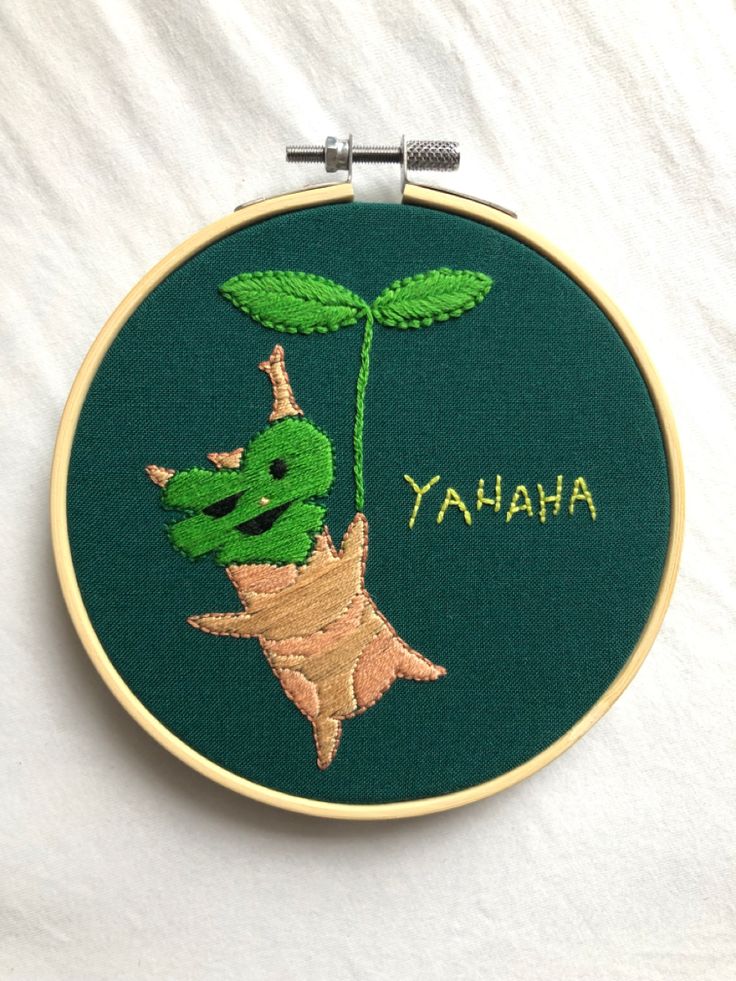 a green embroidered wall hanging with the word ahana on it and an image of a plant