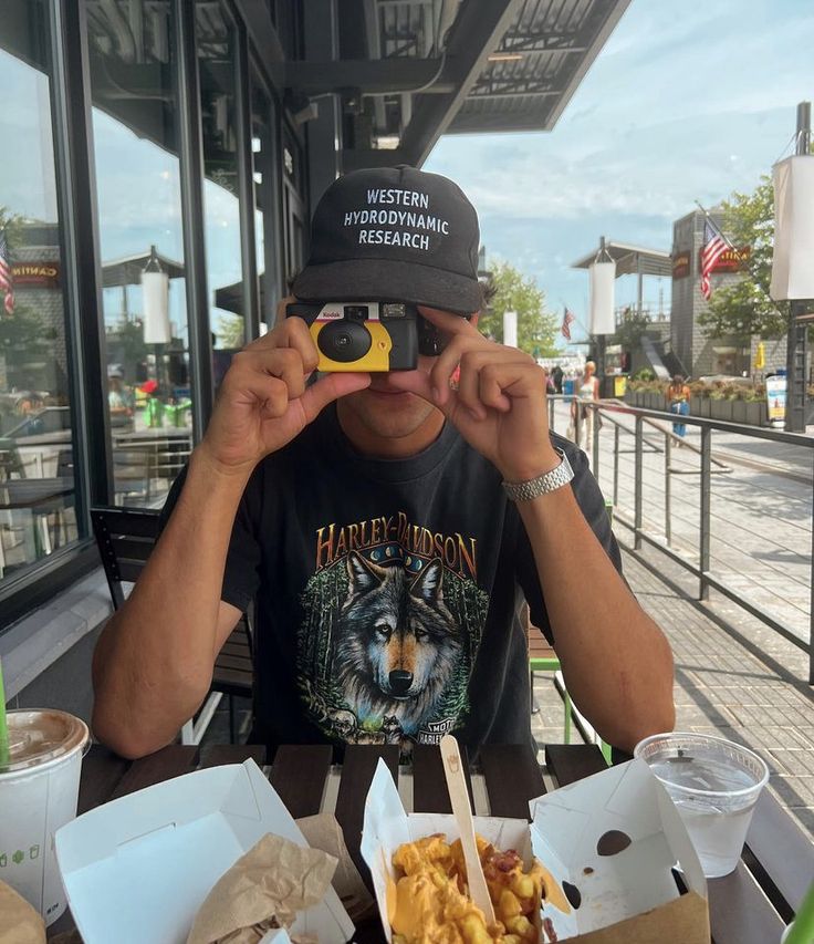 a man sitting at a table with food and bins in front of him looking through binoculars