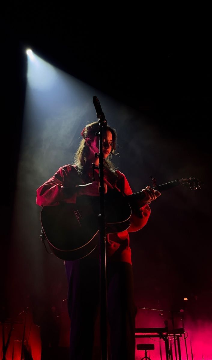 a man holding a guitar while standing in front of a microphone on top of a stage