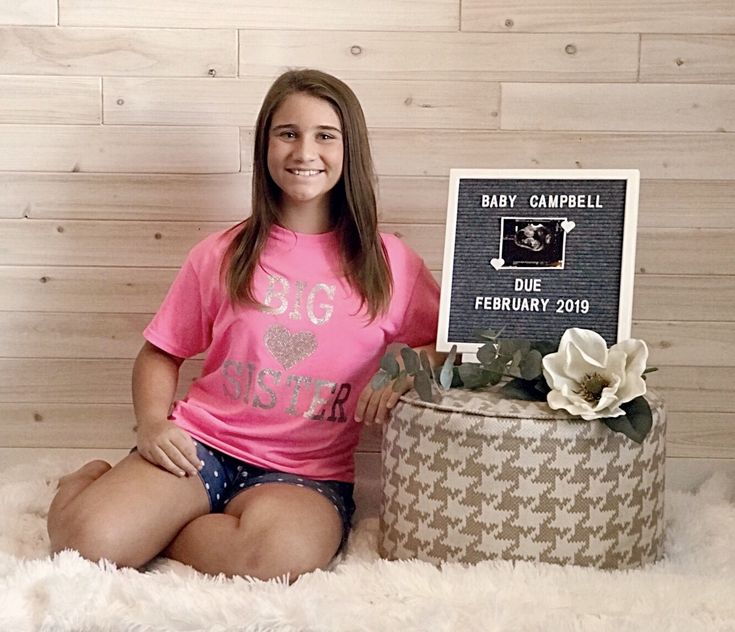 a woman sitting on the floor next to a suitcase with a sign that says baby campbell due february 2009