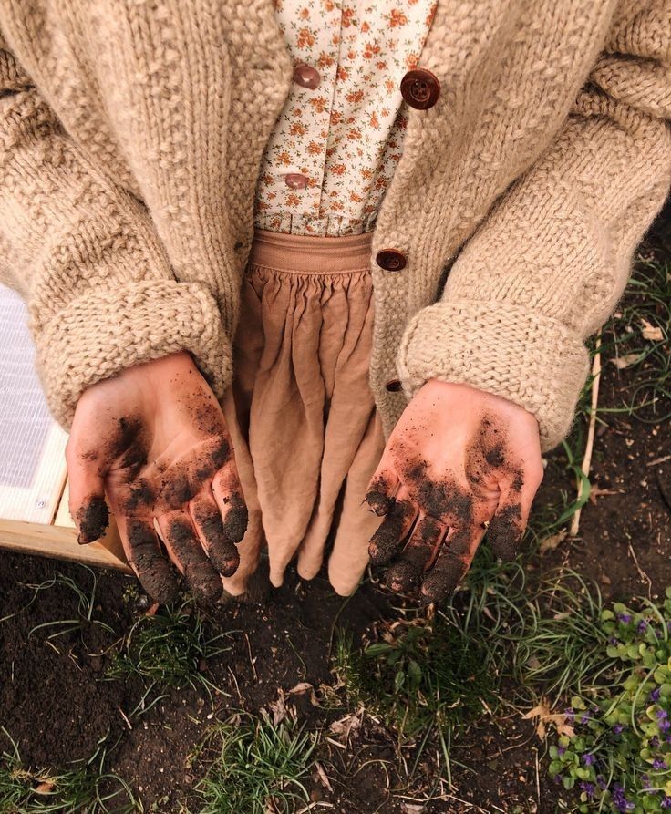 a person with dirty hands holding an open book in the grass and dirt on their hands