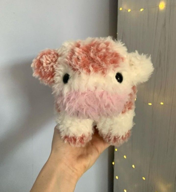 a hand holding a pink and white stuffed animal in front of a wall with lights