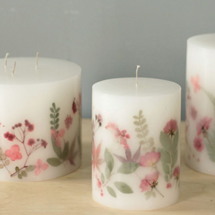 three white candles with floral designs on them sitting on a wooden table next to each other