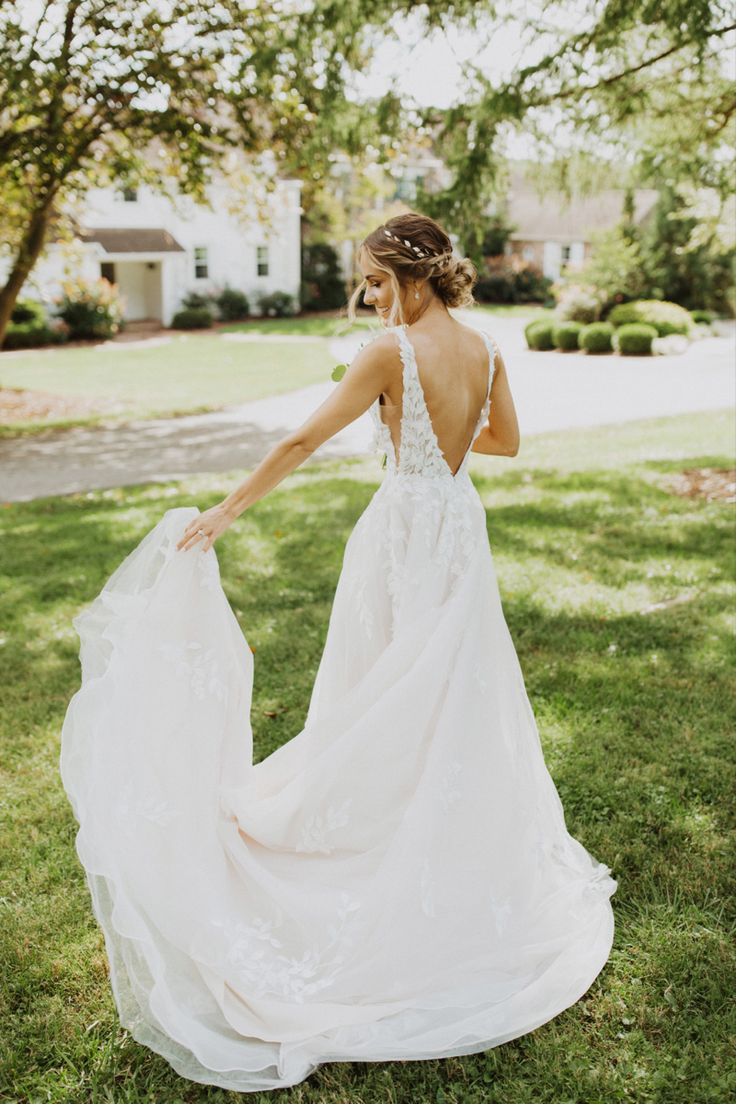 a woman in a wedding dress is walking through the grass with her back to the camera