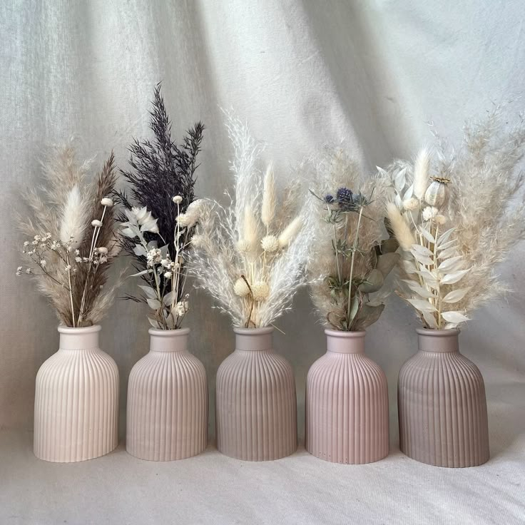 four pink vases with dried flowers in them