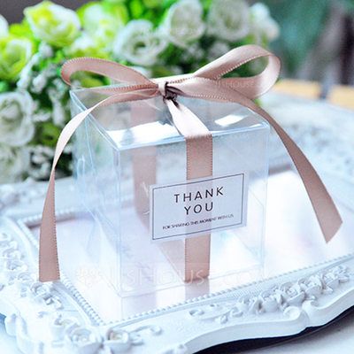 a clear box with a pink ribbon on top of a white tray next to flowers