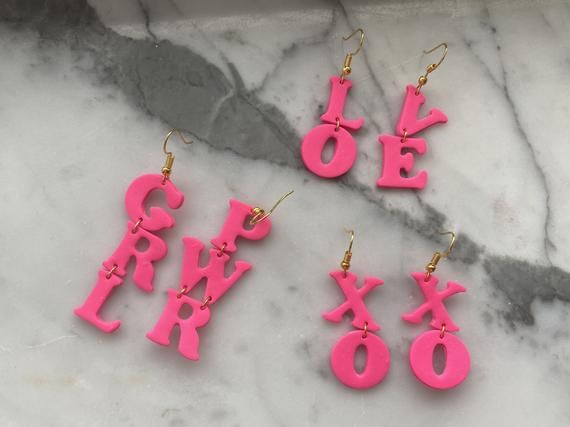 four pink earrings with the word love spelled out in large letters on a marble surface