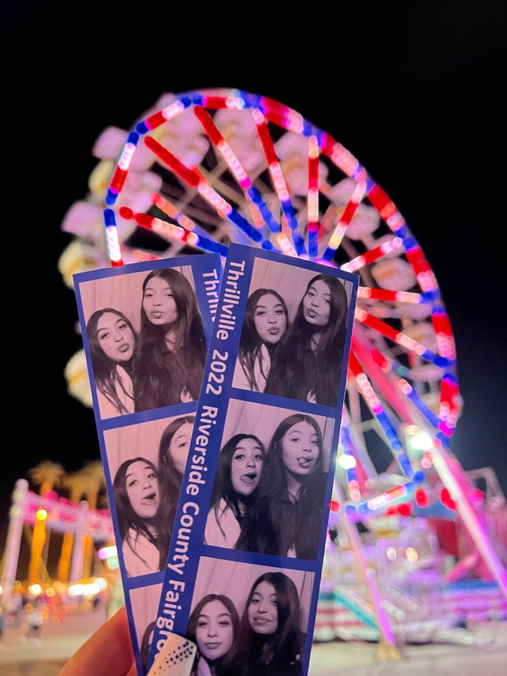 a person holding up two tickets in front of a ferris wheel