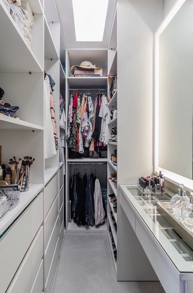 a walk in closet filled with lots of white drawers and shelves next to a mirror