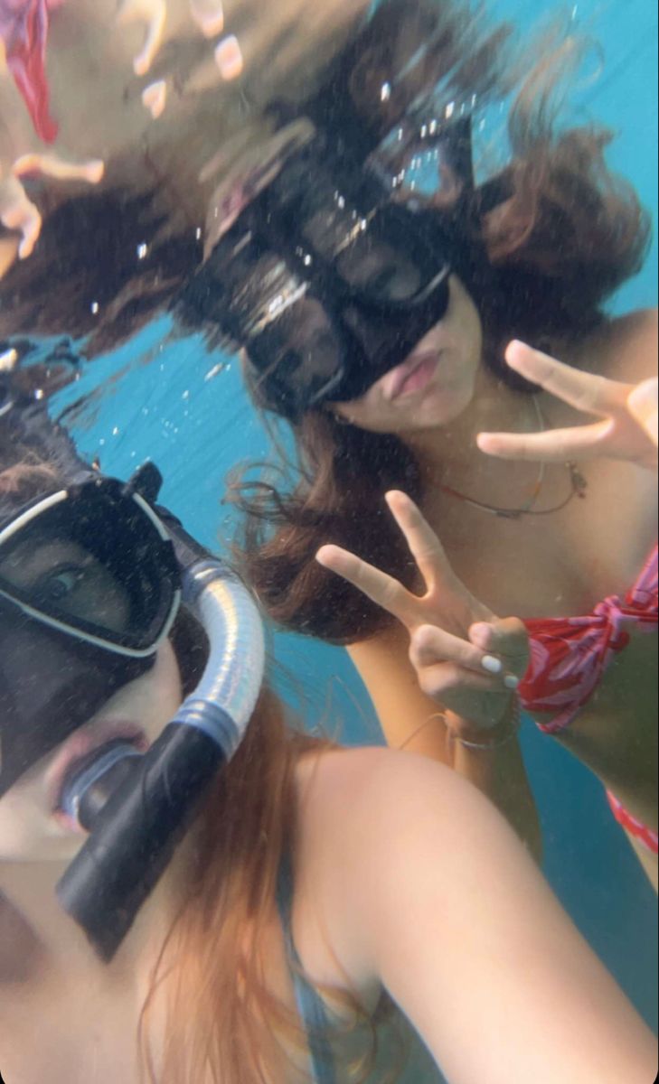 two women wearing snorkels are swimming in the water and making peace signs with their hands