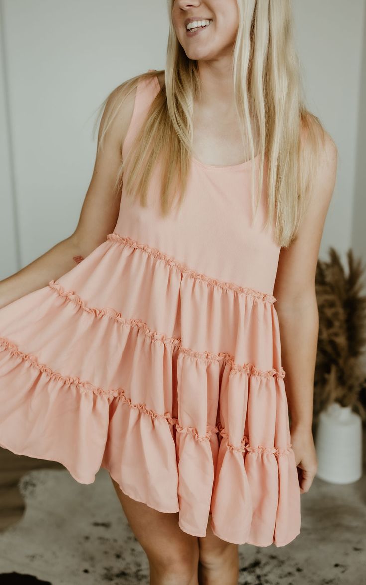 Step into carefree vibes with the Sundown Serenade Tiered Babydoll Dress. Made from textured crepe fabric, this boho-inspired dress features tiered ruffles for a playful, flowy silhouette that dances with every step. The adjustable tie straps allow for a customizable fit, making it perfect for sunny beach days or warm nights out. With its wide bottom sweep, this dress adds an effortlessly feminine touch to any occasion. Whether you're strolling through a farmers' market or heading to a casual su Pink Ruffle Dress For The Beach, Pink Summer Ruffle Dress For Vacation, Pink Tiered Sundress For Beach, Pink Feminine Tiered Beach Dress, Flowy Summer Tiered Dress For Day Out, Cute Vacation Dresses With Ruffles, Flowy Tiered Summer Dress For Day Out, Cute Vacation Dress With Ruffles, Flowy Tiered Dress For A Summer Day Out