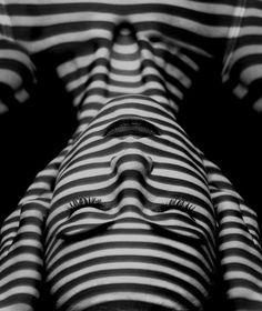 black and white photograph of a woman's face with stripes on her shirt, looking up at the camera