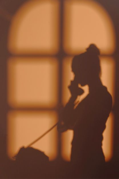 the silhouette of a woman talking on her cell phone in front of an open window