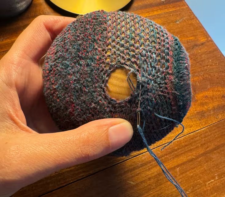 a hand holding a piece of yarn with a hole in the middle that has been sewn