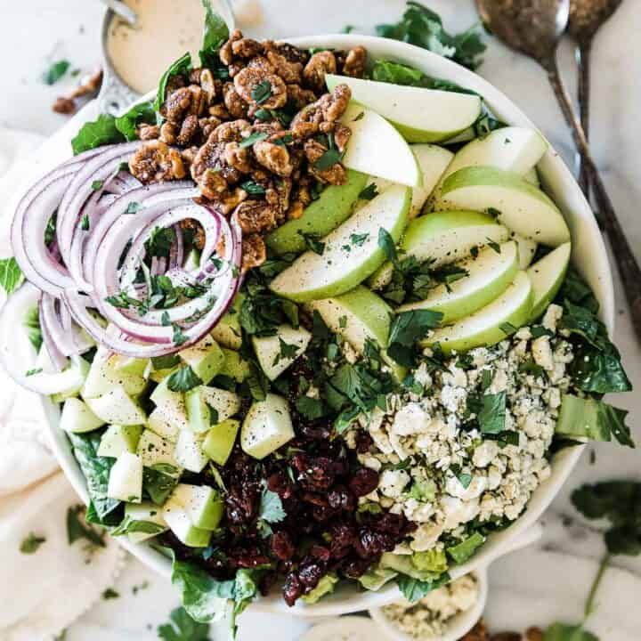 a salad with apples, cranberries, onions and walnuts in a white bowl