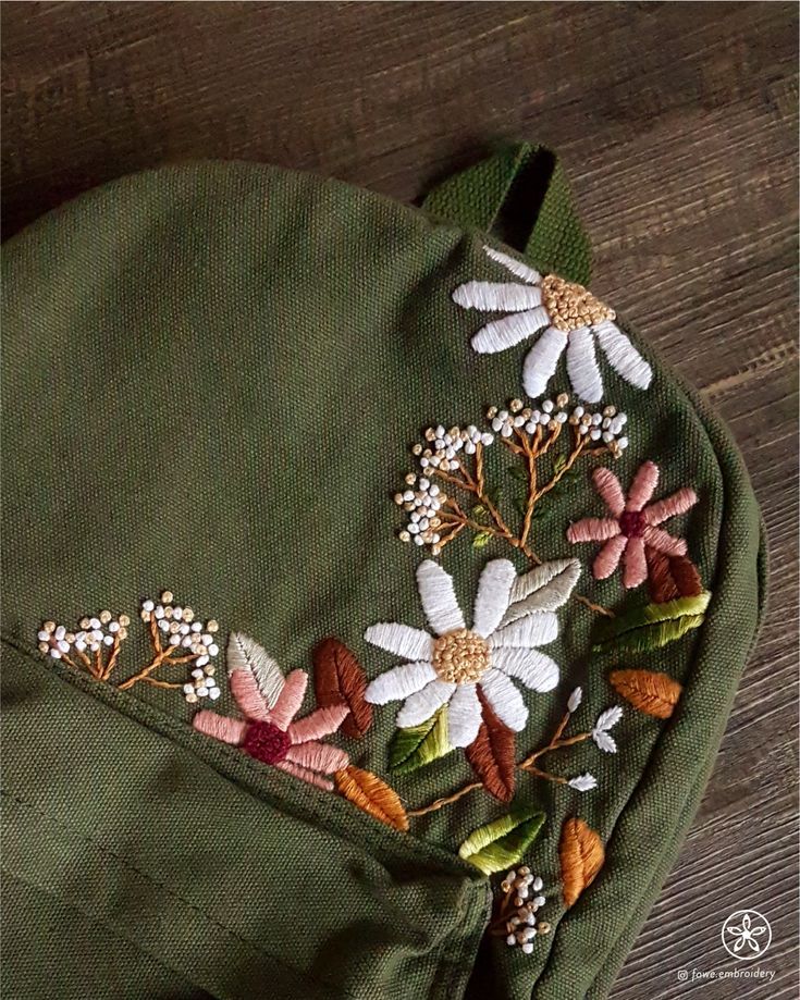 a green bag with white and pink flowers embroidered on it's side, sitting on a wooden floor