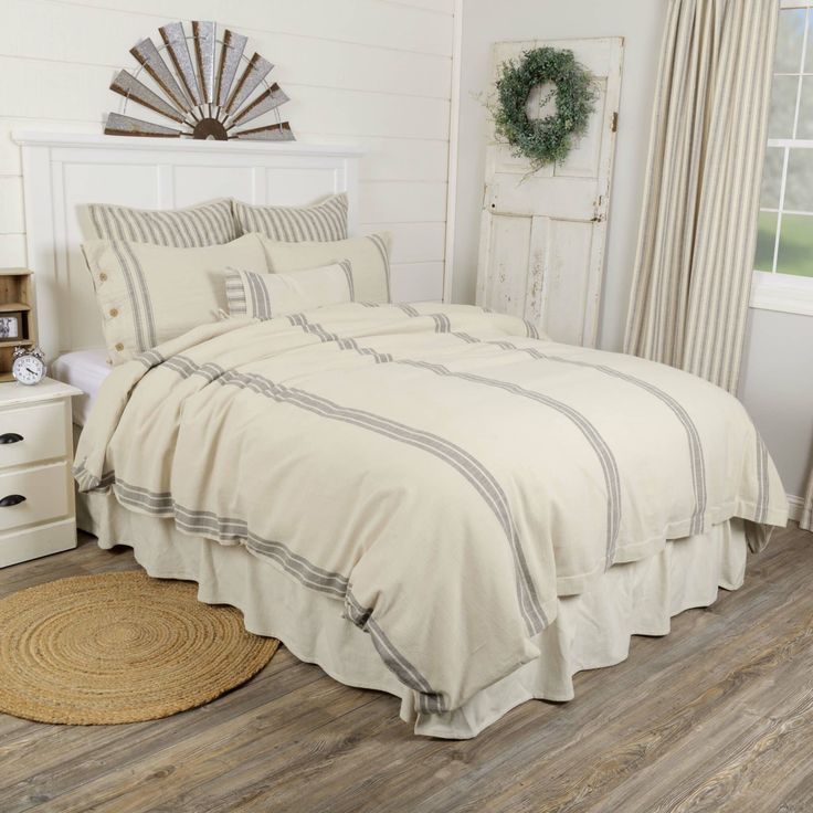 a white bed sitting in a bedroom next to a dresser and window on top of a hard wood floor