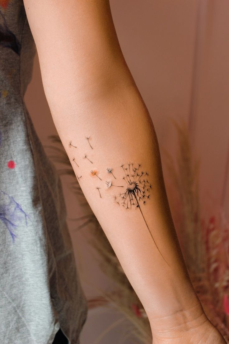 a woman's arm with a dandelion tattoo on it