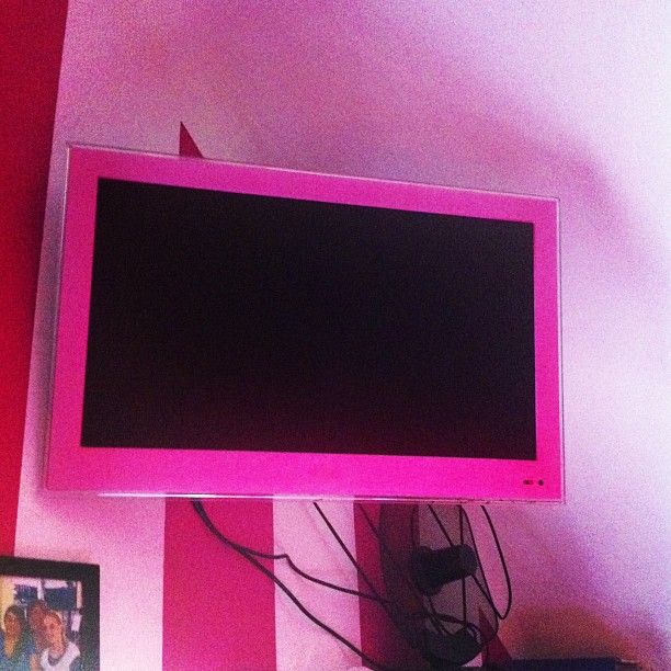 a flat screen tv sitting on top of a wooden table next to a pink wall