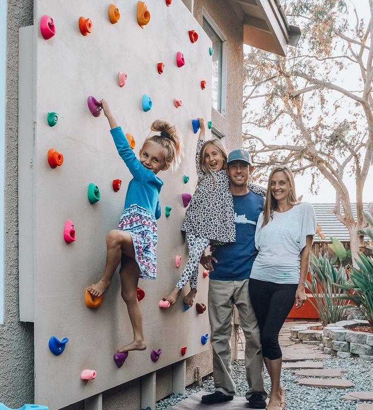 three adults and two children standing in front of a climbing wall