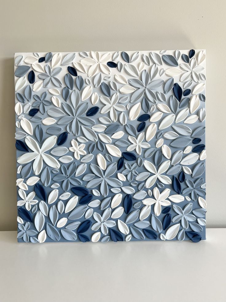 a blue and white painting on a wall with leaves in the center, against a gray background