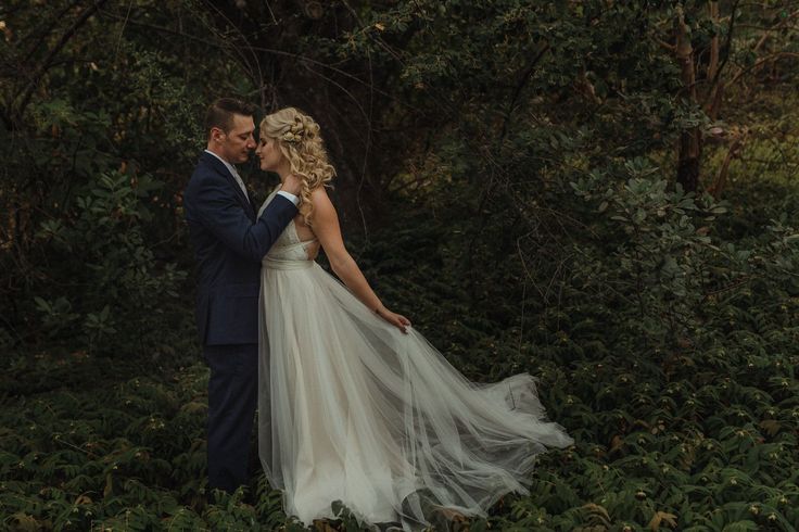 a bride and groom standing in the woods