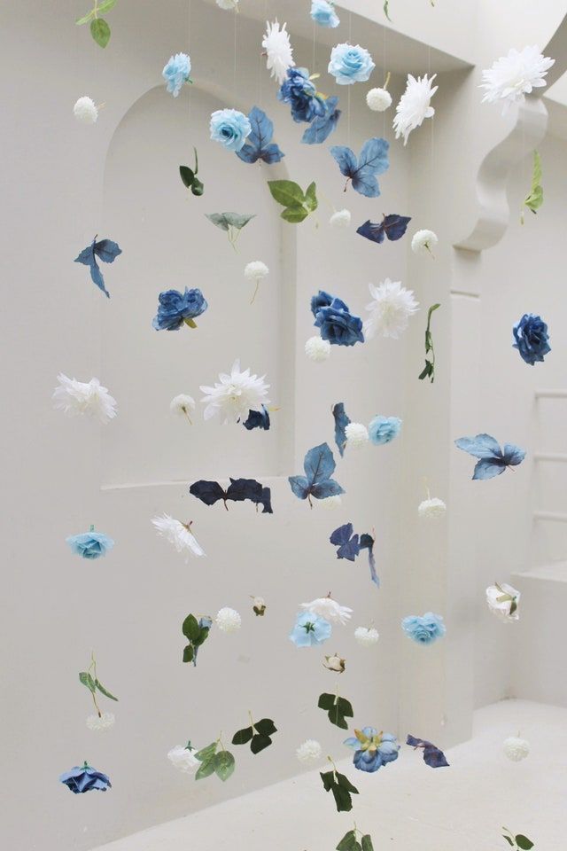 blue and white flowers floating in the air next to a stair case with an open window