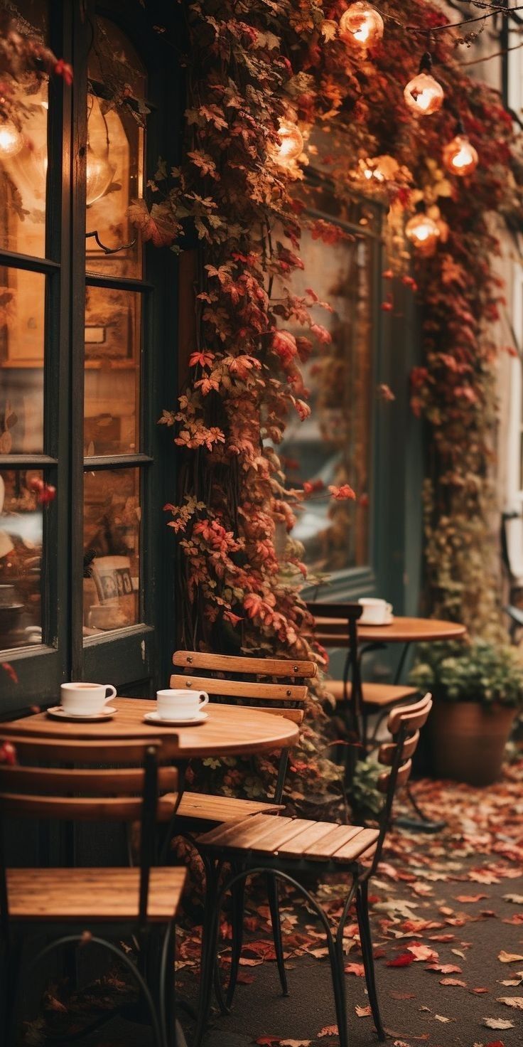 an outdoor cafe with tables and chairs covered in autumn leaves, next to a window