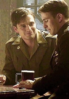 two men in uniform are sitting at a table and one man is holding a mug