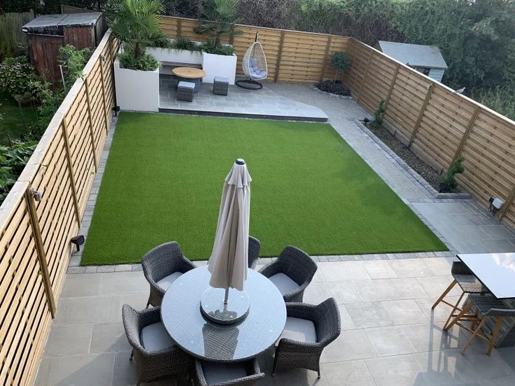 an outdoor patio with table, chairs and umbrella in the grass next to a wooden fence