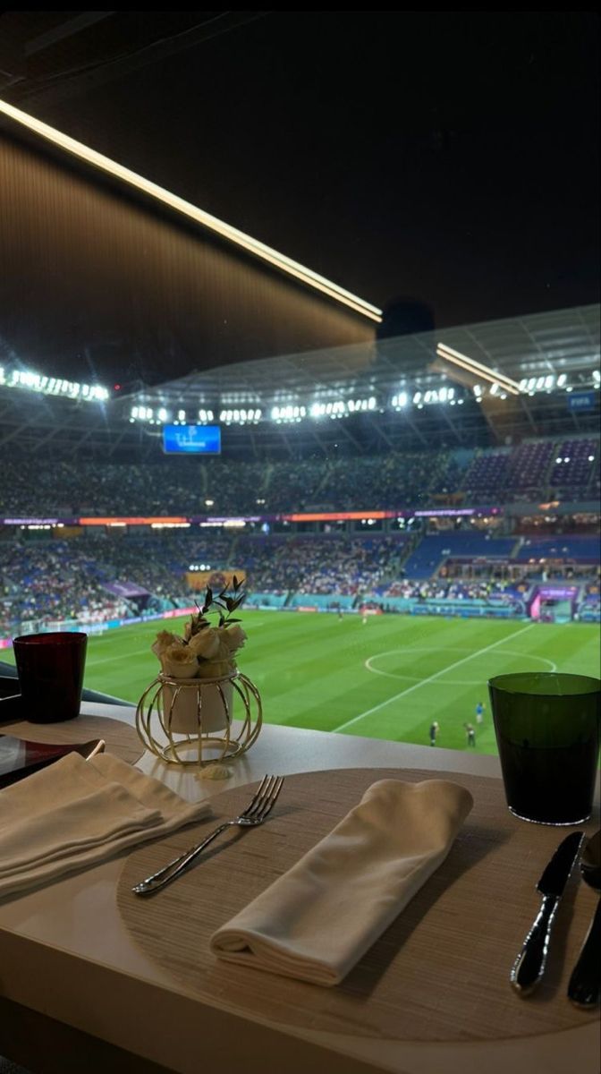 a table set with silverware and napkins in front of a view of a soccer stadium