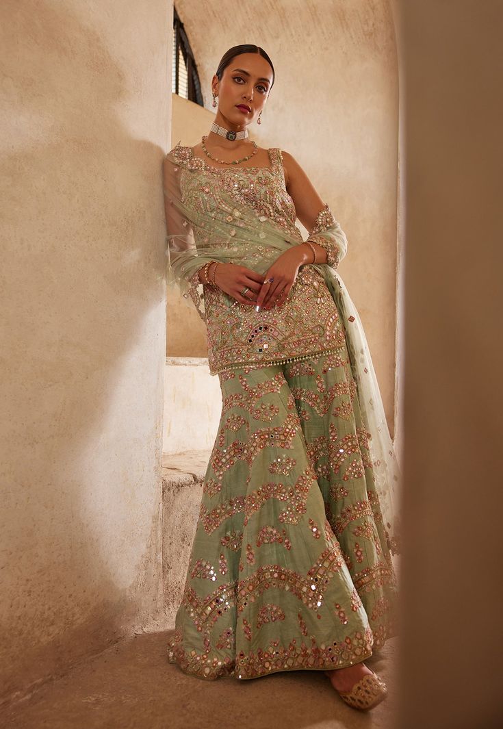 Dive into elegance with this mesmerizing sea green raw silk sharara set. The fully embroidered kurta, adorned with resham, mirror, sequin, and zardosi embroidery, exudes opulence and charm. Paired with a chevron sharara, this ensemble offers a perfect blend of traditional craftsmanship and contemporary design. Embrace sophistication and make a statement with this timeless piece. Raw Silk Sharara, Bridal Gharara, Green Sharara, Silk Sharara, Embroidered Sharara, Mehendi Outfit, Zardosi Embroidery, Bride Sister, Indian Couture