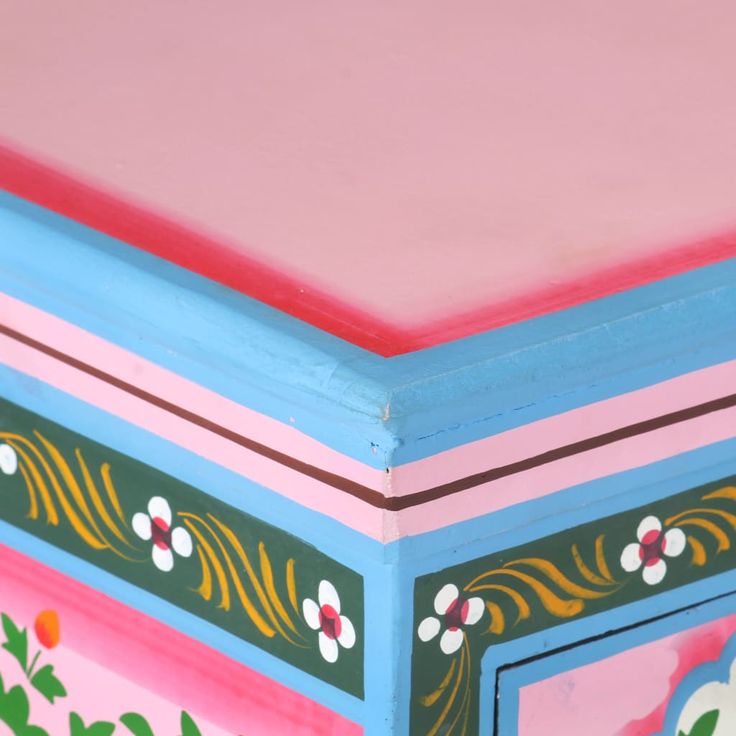 a painted wooden box with flowers and leaves on the sides, sitting against a pink background