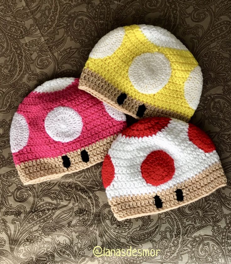 two crocheted mushroom hats sitting on top of a bed next to each other