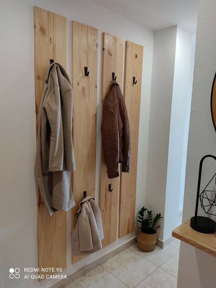 the coat rack is made out of wood and has three coats hanging from it's hooks