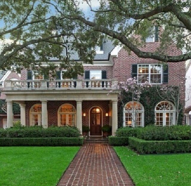 a brick walkway leads to the front entrance of a large house with trees and bushes