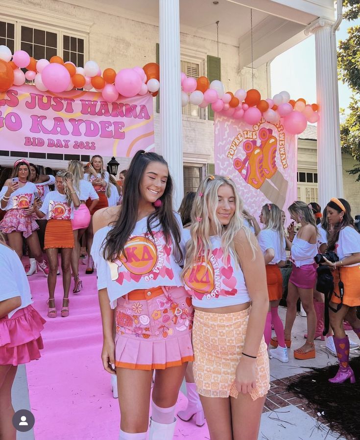 two girls in pink and orange outfits standing next to each other on a pink carpet