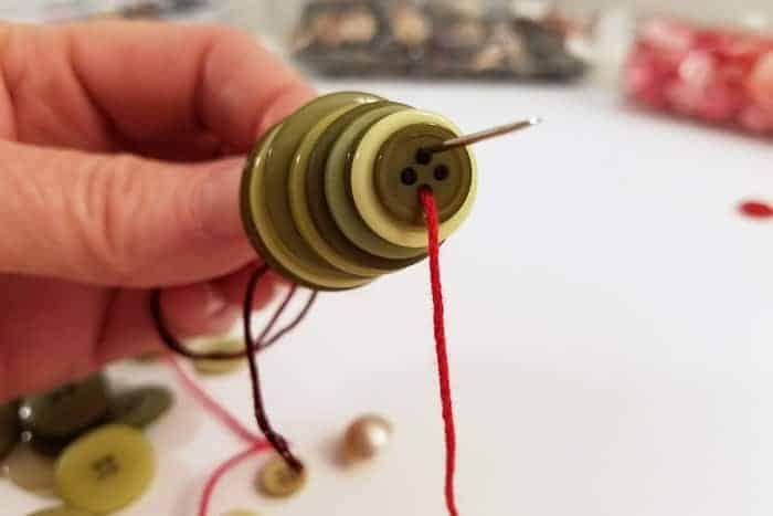 a hand holding a sewing needle and thread with buttons on the table next to it