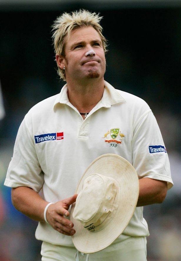 a man wearing a white shirt and hat standing on a field with his hands in his pockets