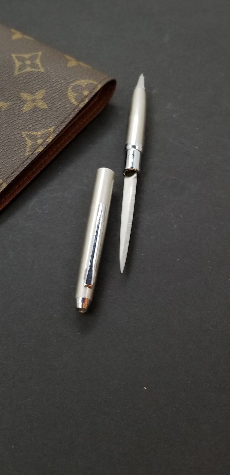 two pens sitting on top of a table next to an envelope and pen holder with the word louis vuitton written on it