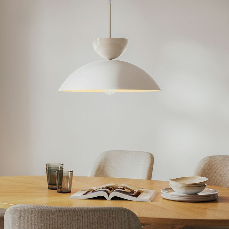 an open book on a wooden table with white chairs and a light fixture above it