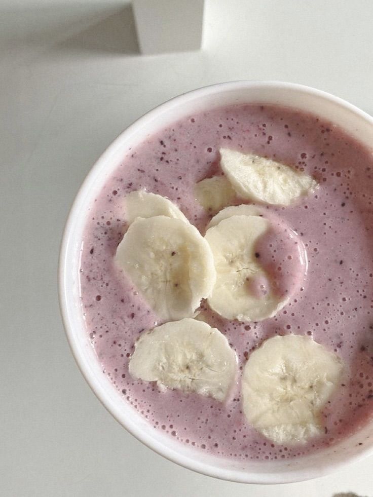 a white bowl filled with purple liquid and sliced banana slices in it on top of a table