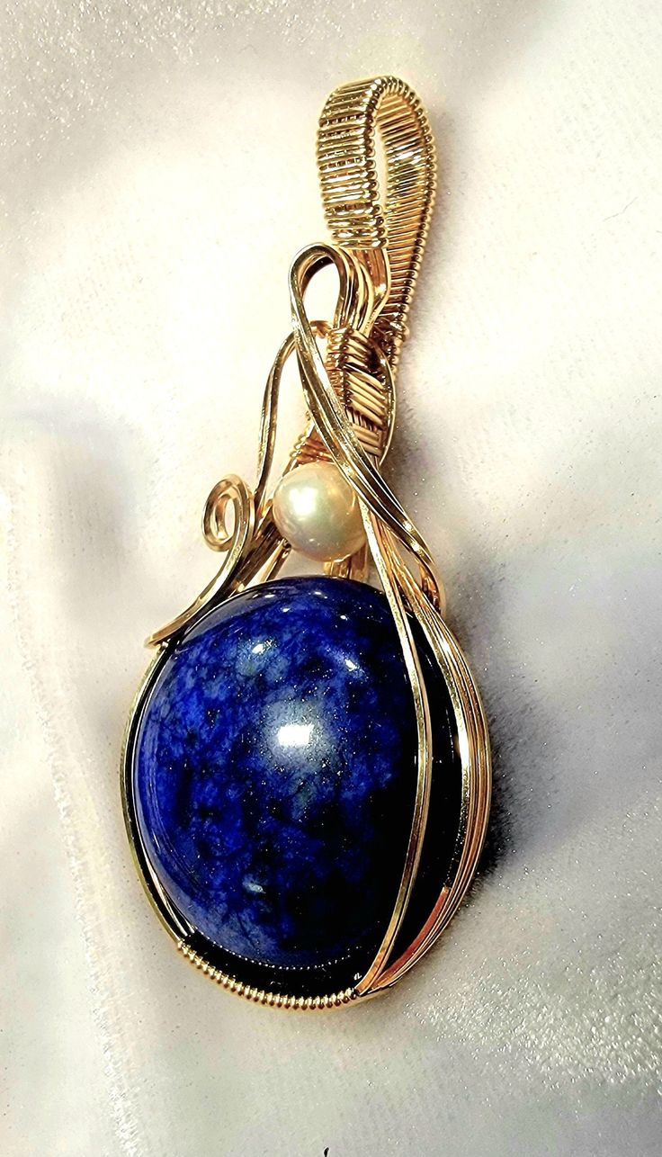 This beautiful Lapis gemstone with an Akoya Pearl accent is artfully hand wire wrapped in 14K (14/20) gold filled wire.  The pendant measures 2 3/8 inches in length and is 1 1/8 inch wide.  The bail is generously sized in order to accommodate a variety of chain widths. A handcrafted pendant and a beautiful Lapis and Pearl,  it is one of a kind. A gift box is included. Note of Interest: Wire wrapping can be traced back to several ancient civilizations such as the Vikings, Celts, and the Egyptians.  Some believed that wire-wrapped jewelry had magical and spiritual properties and it was used in many rituals and ceremonies, particularly with the Celts. Yellow Gold Wire Wrapped Pendant Jewelry, Wire Wrapped Yellow Gold Pendant Jewelry, Artisan Oval Hand-wrapped Jewelry, Artisan Hand Wrapped Oval Jewelry, Gold Oval Wire Wrapped Necklace, Oval Gold Wire Wrapped Necklaces, Oval Gold Wire Wrapped Necklace, Elegant Copper Wire Pendant Jewelry, Elegant Hand Wrapped Pendant Jewelry