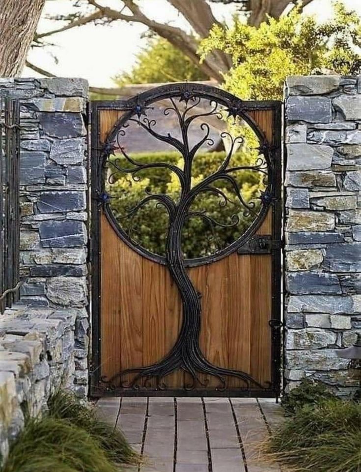 an iron gate with a tree in the center and stone walls around it, leading to a wooden door