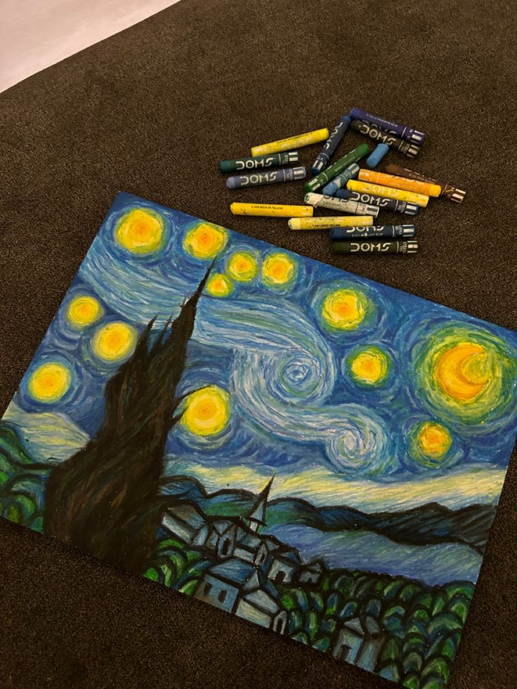 some crayons are laying on the ground next to an art project that looks like starry night