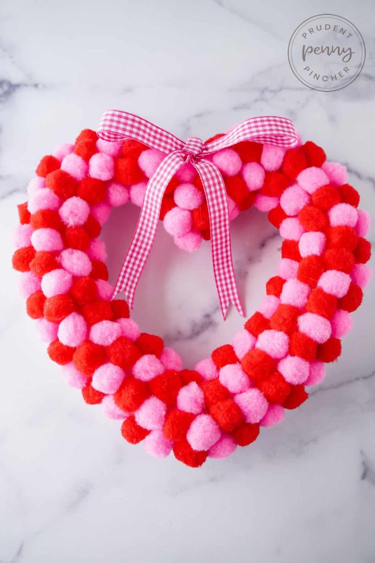 a red and pink heart shaped wreath with pom - poms on the front