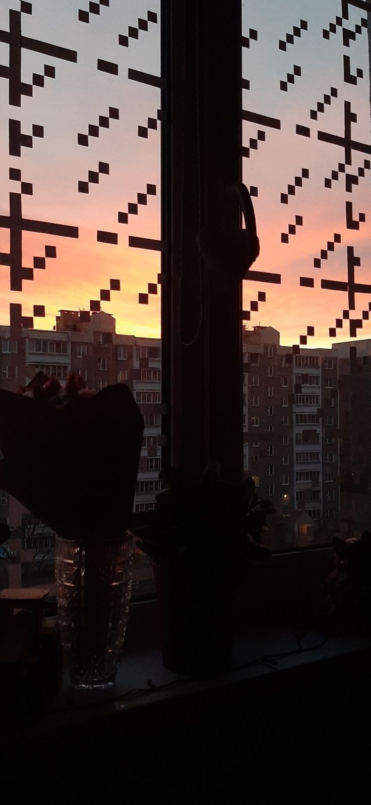 the sun is setting over some buildings and water in front of a window with many crosses on it