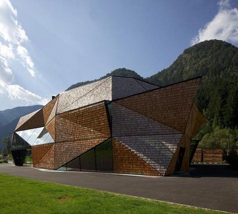 an unusual building in the middle of a green field with mountains in the back ground